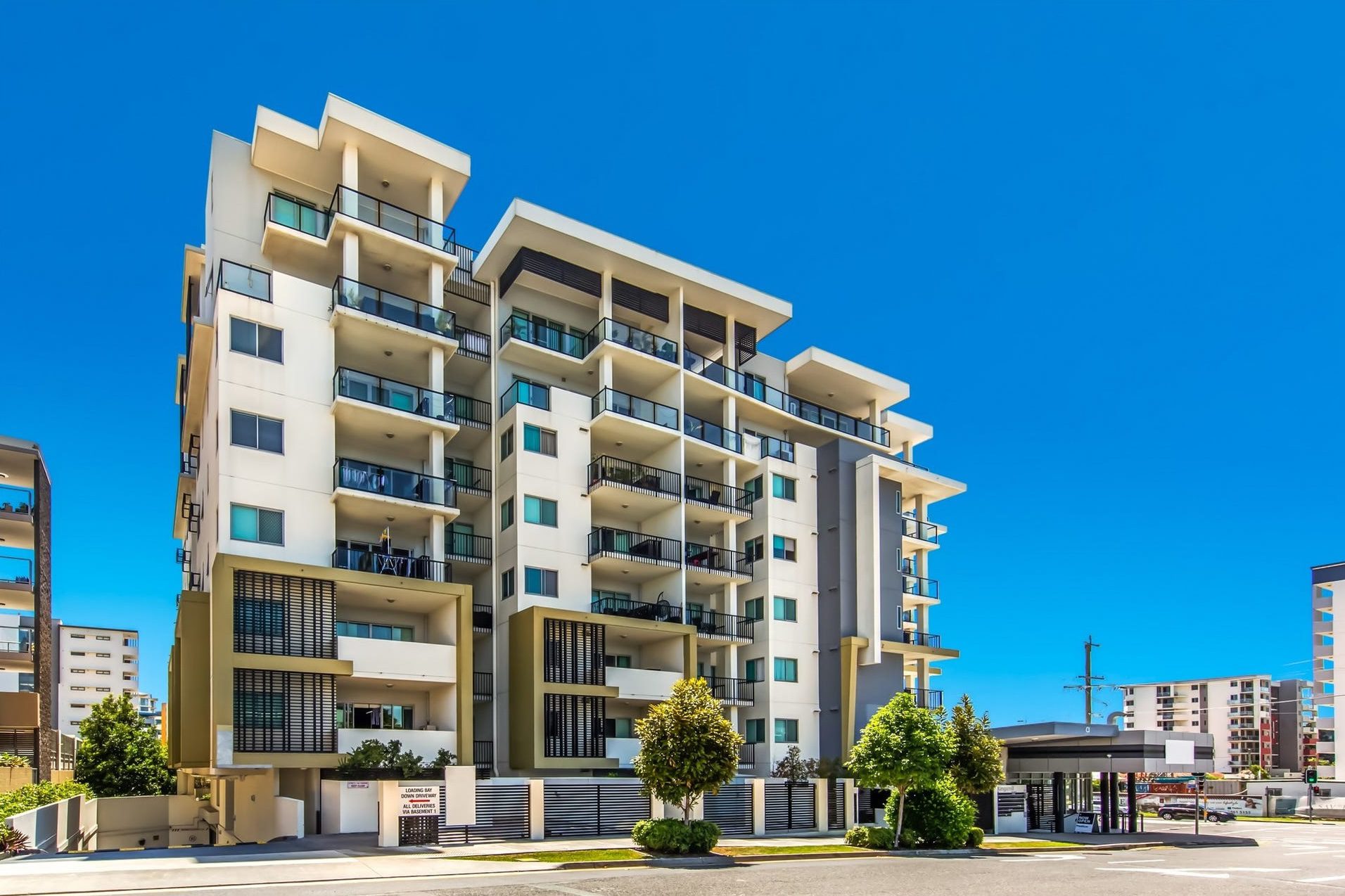 Modern apartment building with multiple levels and balconies under a clear blue sky.